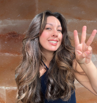 woman holding 3 fingers up in front of a salt brick wall